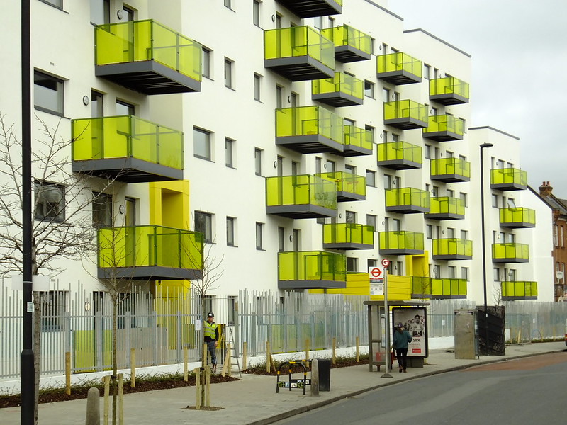 Photo is of a housing association building in London in 2012, a block of flats with balconies made from yellow translucent materials outside every second window.